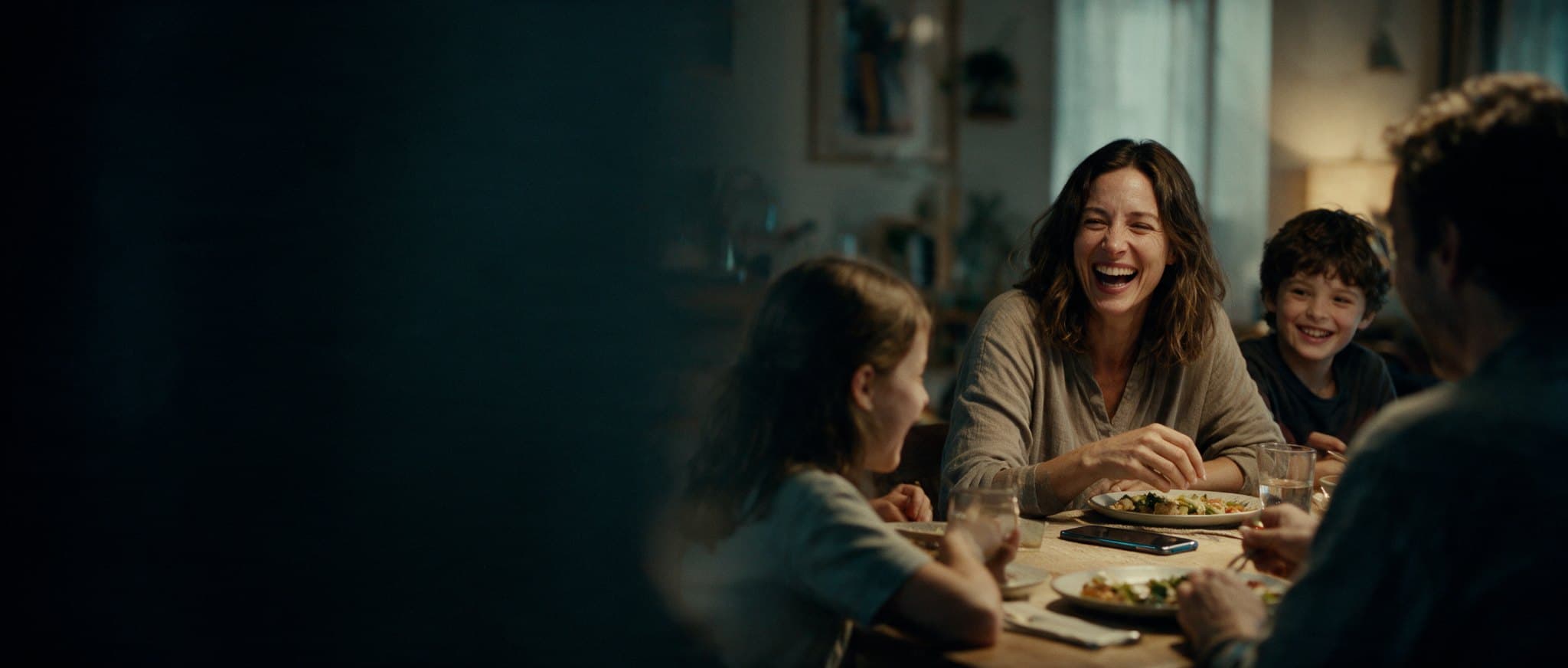 A family laughing at dinner, a phone face down beside a plate